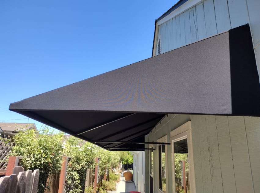 A stylish black awning is positioned over a house with a white roof, providing shade and enhancing the residential facade.