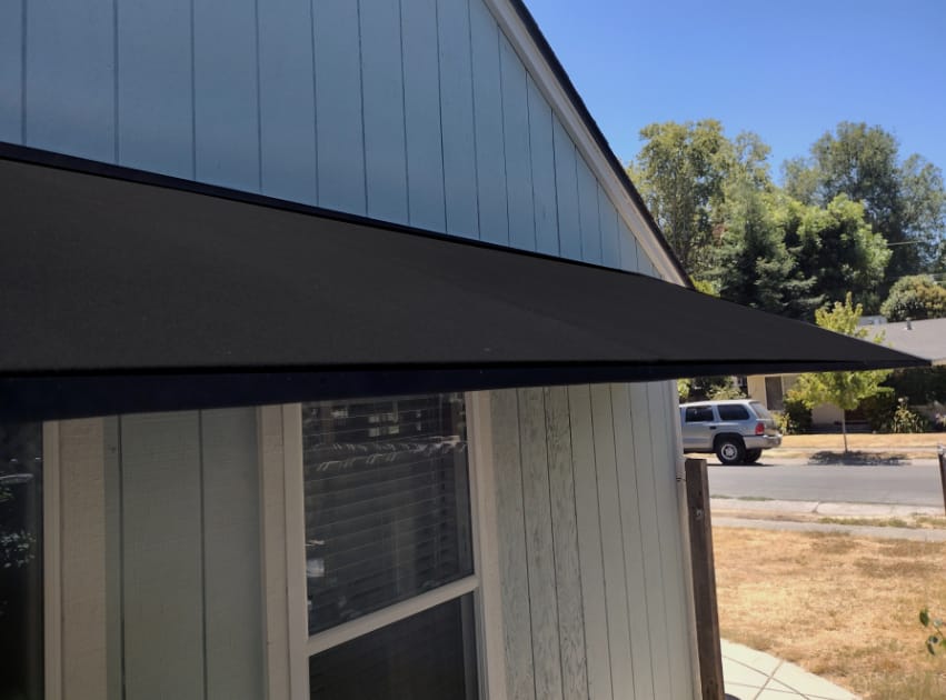 A black awning adorns a residential home, providing shade above a white window.